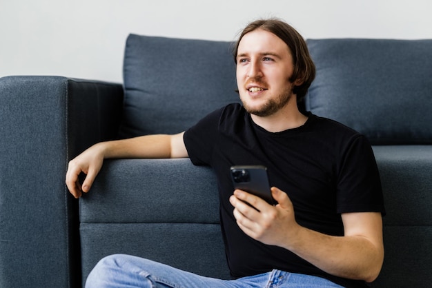 Attractive young man sitting on a floor in the living room using mobile phone