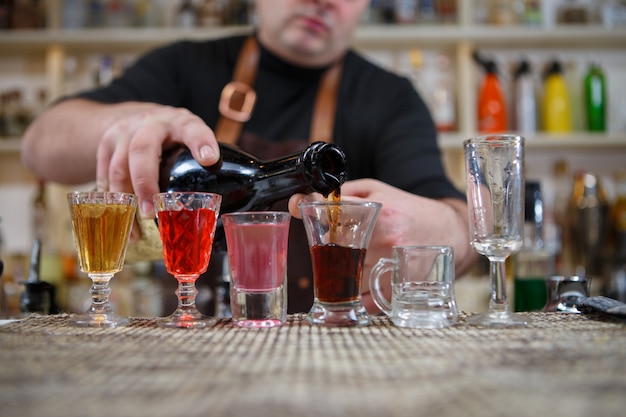 Foto il barista versa varie bevande alcoliche in piccoli bicchieri al bar