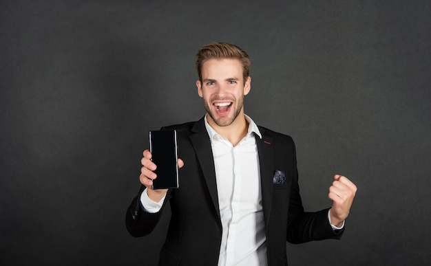 Будьте в выигрыше Счастливый бизнесмен держит мобильный телефон, делая выигрышный жест Выиграйте смартфон