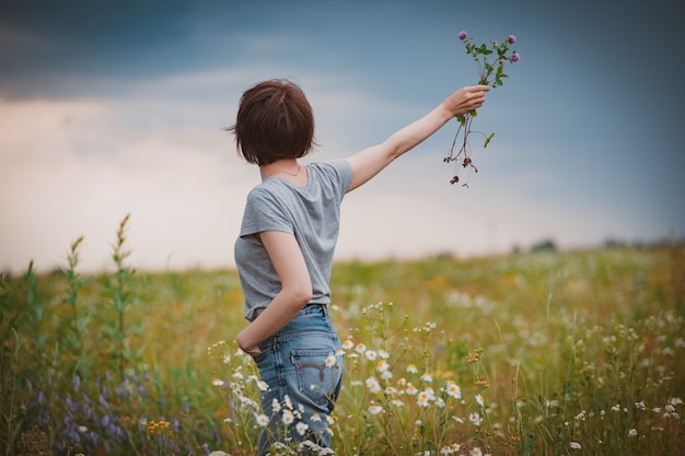 Красивая молодая девушка в поле цветов наслаждается ароматом и видом полевых ромашек.