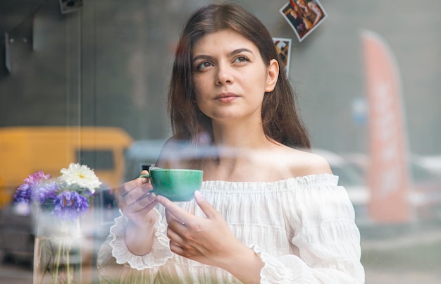 Красивая молодая женщина в кафе с видом на чашку кофе с улицы