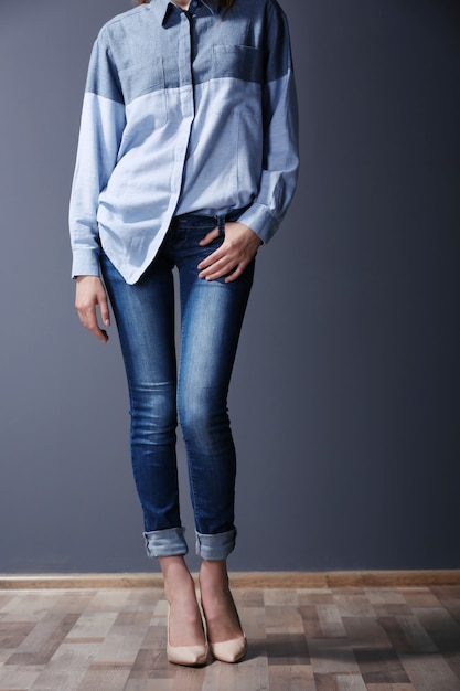 Photo beautiful young woman in shirt and jeans on grey wall
