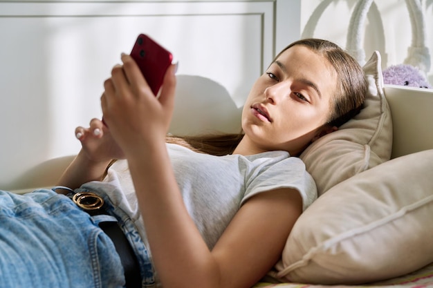 Красивая молодая девушка-подросток отдыхает на диване с помощью смартфона
