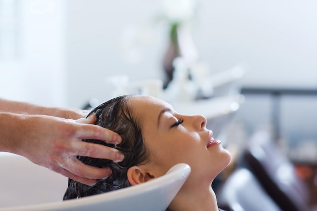 Photo beauty and people concept - happy young woman with hairdresser washing head at hair salon