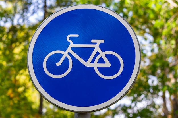 Знак велосипеда на фоне зеленой солнечной листвы Сине-белый знак велосипедной дорожки, указывающий велосипедный маршрут