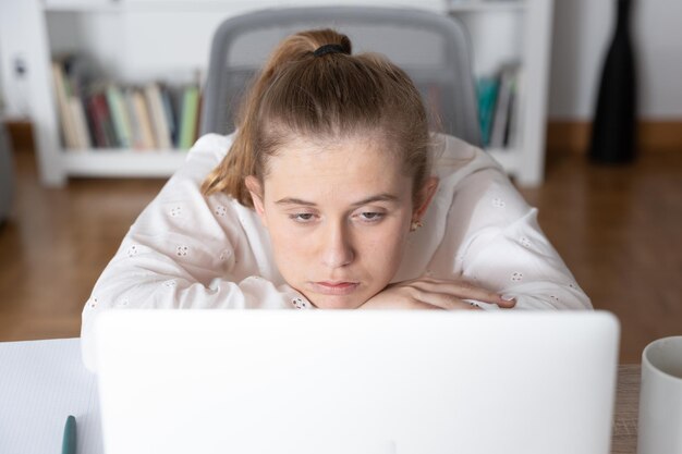 Bored female student in front of laptop paying attention to virtual class