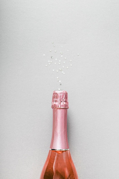 Фото Бутылка розового шампанского и конфеты на сером фоне минималистическая вертикальная рождественская и новогодняя открытка