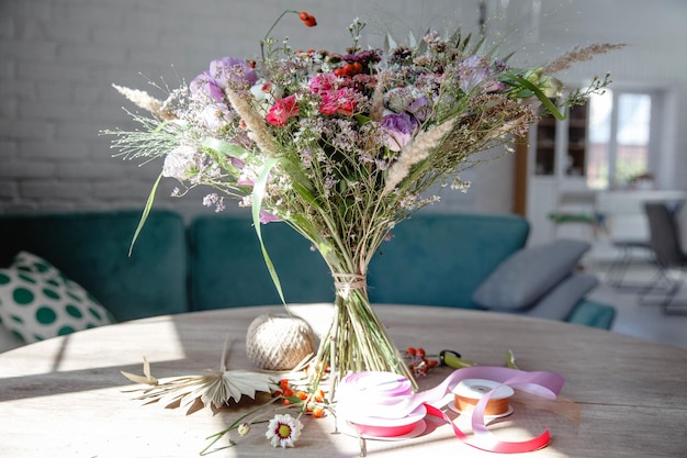 Букет из разных цветов и трав, перевязанных ниткой, на круглом деревянном столе с цветочной ак...