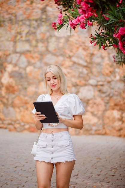 Blonde girl is holding planshet in white dress on stone background