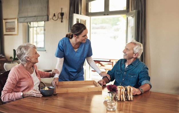 Фото Завтрак подается с широкой улыбкой, это пятизвездочный сервис. снимок молодой медсестры, проверяющей пожилую пару во время завтрака в доме престарелых.