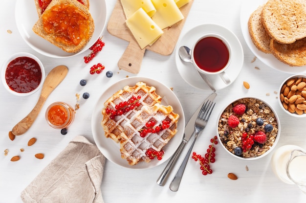Breakfast with granola berry nuts, waffle, toast, jam, chocolate spread and coffee. Top view