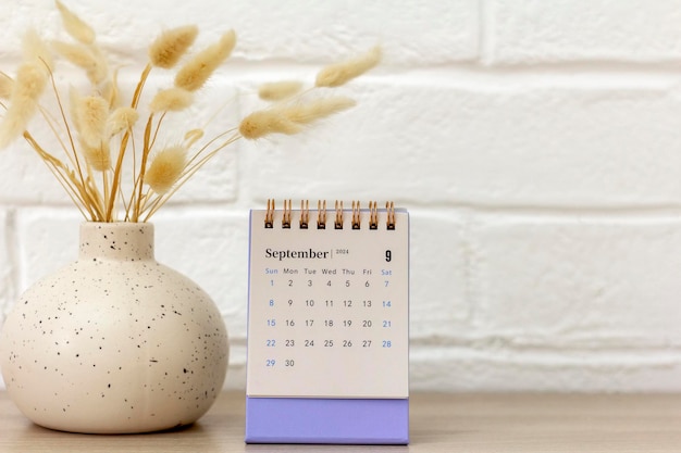 Calendar for September 2024 and a vase with dried flowers on the table