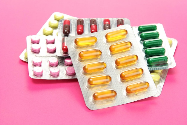 Капсулы и таблетки, упакованные в волдыри на розовом фоне
