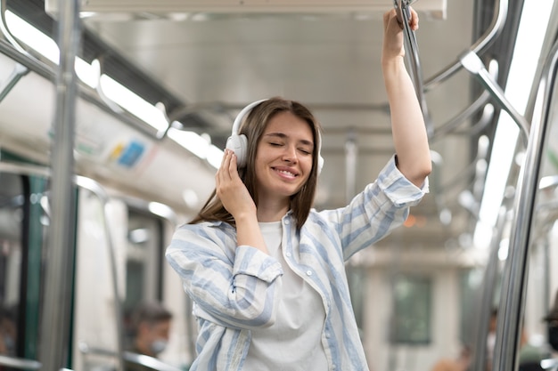 Беззаботная миловидная пассажирка из миллениума слушает музыку в беспроводных наушниках в поезде метро