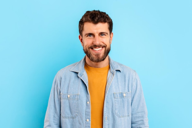 Photo cheerful young bearded man standing against blue studio background