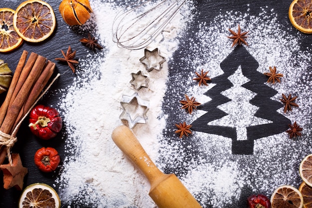 Рождественская кулинария: елка из муки на темном столе, ингредиенты для выпечки и сухофрукты на темном фоне, вид сверху