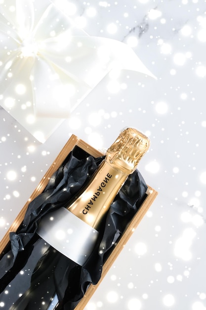 Фото Рождественская бутылка шампанского и подарочная коробка и блестящий снег на мраморном фоне