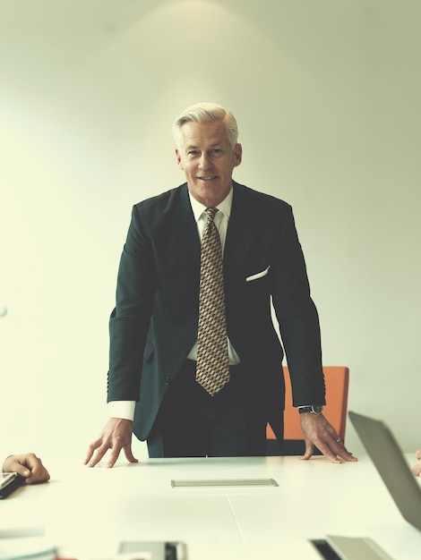 Foto uomo d'affari anziano fiducioso e bello in piedi dietro il tavolo nella sala riunioni dell'ufficio moderno