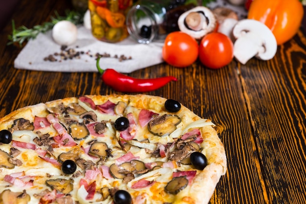 나무 테이블에 햄, 양파, 올리브, 토마토, 버섯 및 기타 야채를 배경으로 하는 맛있는 피자 클로즈업