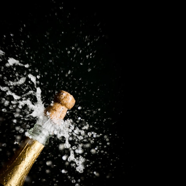 Фото Клоуз-ап шампанского, брызгающего из бутылки на черном фоне