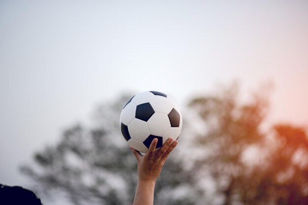 Фото Рука, держащая футбольный мяч против неба.