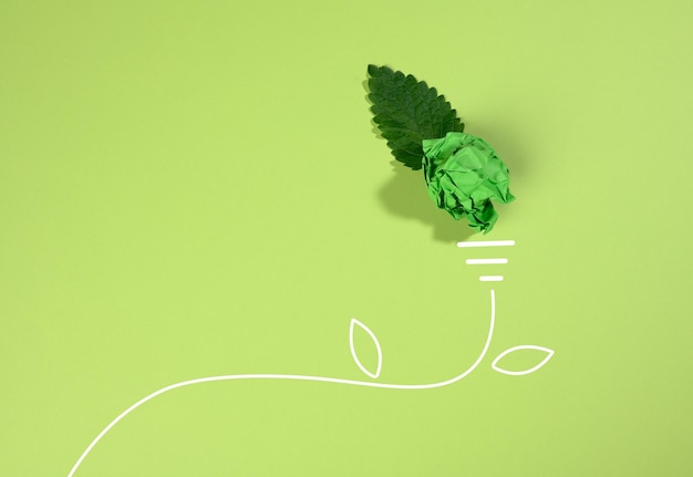 Foto un foglio di carta arrugginito e una foglia verde su uno sfondo verde la forma di una lampadina concetto di risparmio energetico nuova idea creativa