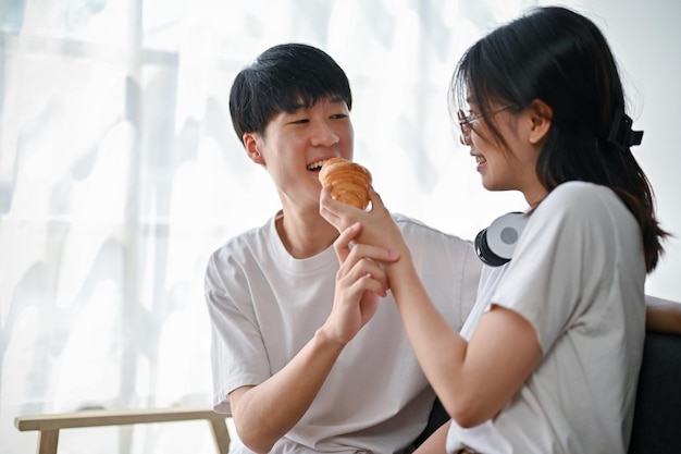 Симпатичная подружка кормит своего парня круассаном Прекрасная молодая азиатская пара