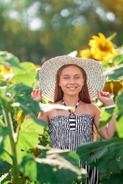 Фото Симпатичная девочка-подросток в широкополой шляпе в поле подсолнухов. концепция летнего времени.