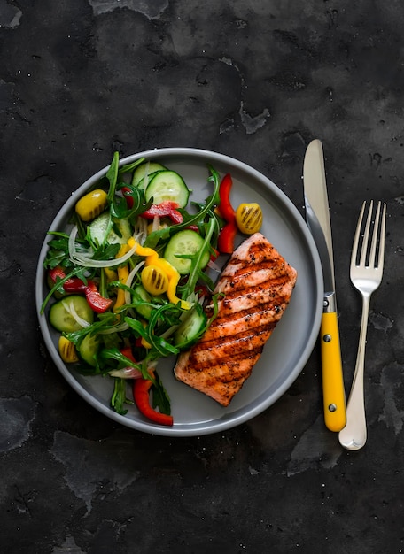 Photo delicious diet lunch dinner grilled salmon and fresh vegetable salad on a dark background top view