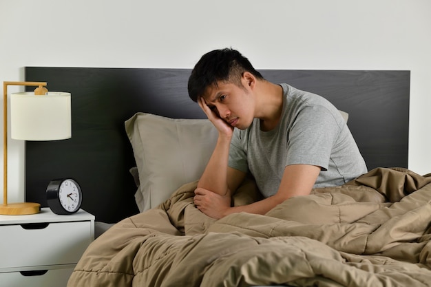 Photo depressed young asian man sitting in bed cannot sleep from insomnia