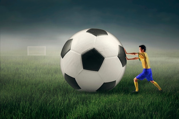 Foto digitale samengestelde afbeelding van een man die een grote voetbal op het veld duwt