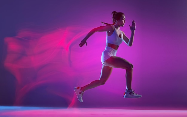 Photo dynamic portrait of young sportive woman training running isolated over purple background in neon with mixed lights