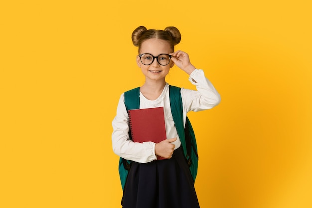 Фото Образовательная концепция портрет милой маленькой школьницы, трогающей очки и держащей в руках рабочие тетради