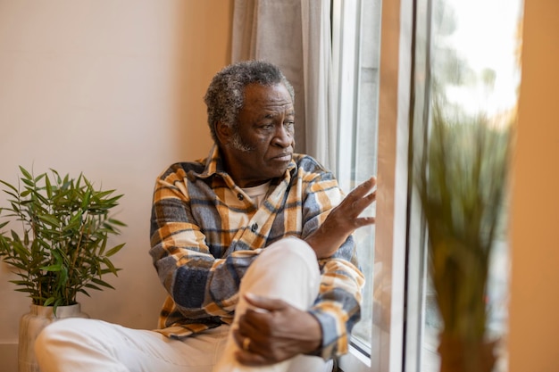 Photo elderly pensioner at home sad looks out the window serious