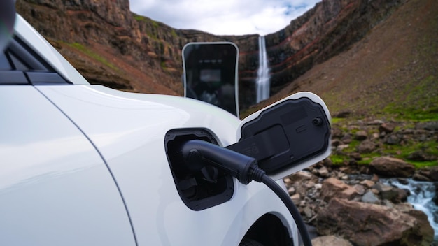 Electric car charging energy from charging station in the natural scenery waterfall and stream background Progressive concept of energy sustainability by EV car powered by renewable energy