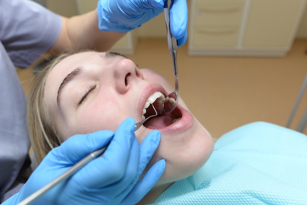 Европейская молодая женщина сидит в медицинском кресле, пока стоматолог лечит зубы в стоматологической клинике Осмотр зубов с помощью стоматологического зеркала