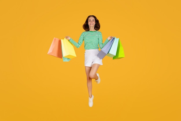 Excited pretty young lady jumping in air with purchases