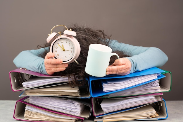 Фото Измученная усталая женщина кофе будильник куча файлов папки выгорание стресс переутомление давление