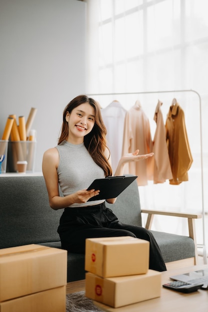 Фото Модная концепция блогера молодые азиатские женщины, продающие одежду по потоковому видео стартап малого бизнеса мсб, использующий смартфон или планшет, принимающий, получающий и проверяющий в офисе