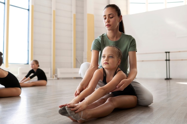 Female ballet trainer helping girl stretch during lesson