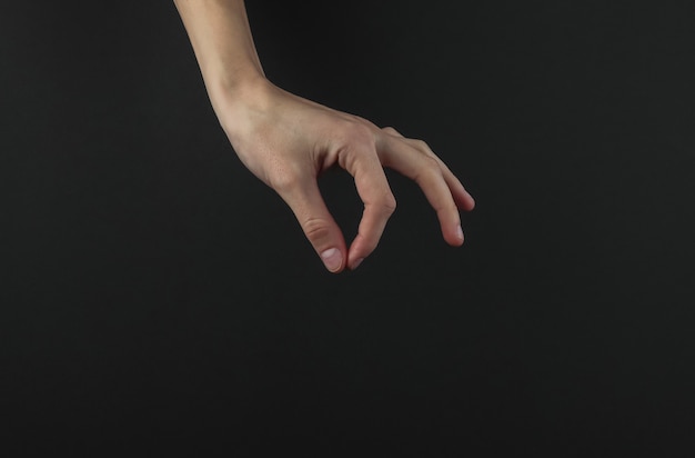 Фото Женская рука с пальцами что-то держит на черном фоне.