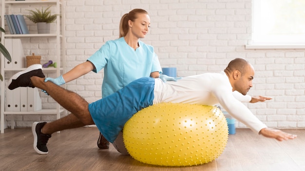 Фото Женский физиотерапевт помогает пациенту мужского пола на мяче