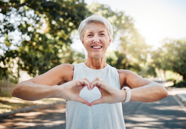 Photo fitness happy and heart hands of old woman in nature after running for health wellness and workout smile motivation and peace with senior lady and sign for love faith and training in nature