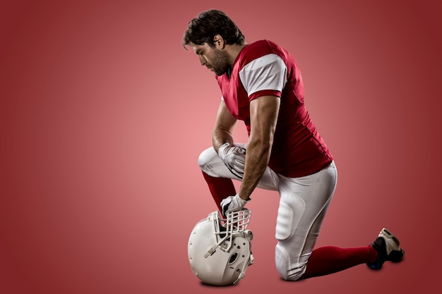 Photo football player with a red uniform on his knees on a red wall