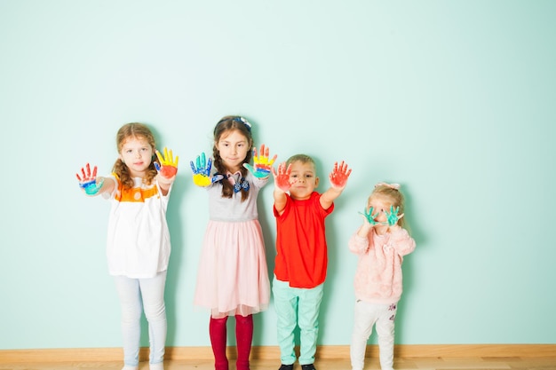 Фото Четыре творческих мальчика и девочки стоят на белом фоне, показывая свои красочные нарисованные руки.