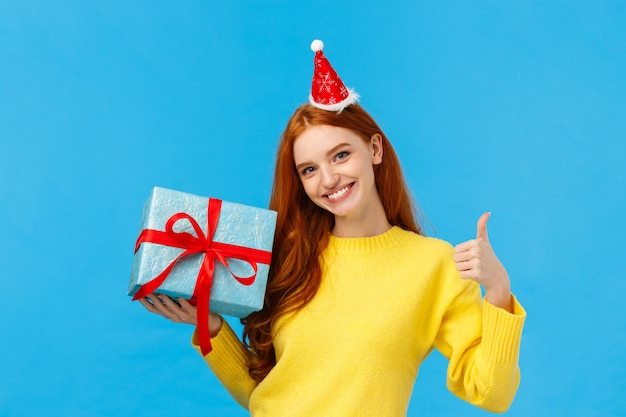 Девушка может легко обернуть твой подарок. Довольный и напористый симпатичный рыжий женский продавец помогает клиенту, показывая большой палец вверх, все сделано или хороший жест, улыбаясь, держа коробку подарка