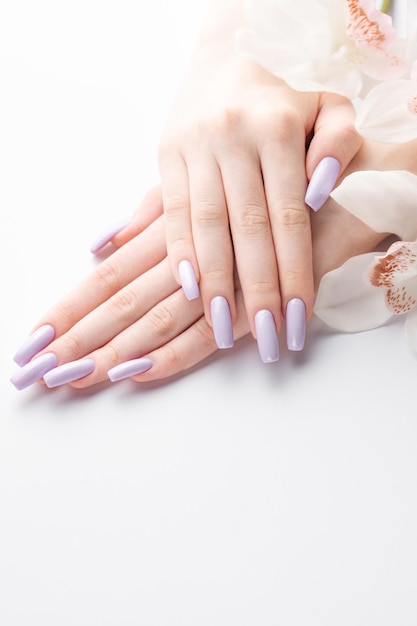 Photo girl's hands with delicate purple manicure and orchid flowers