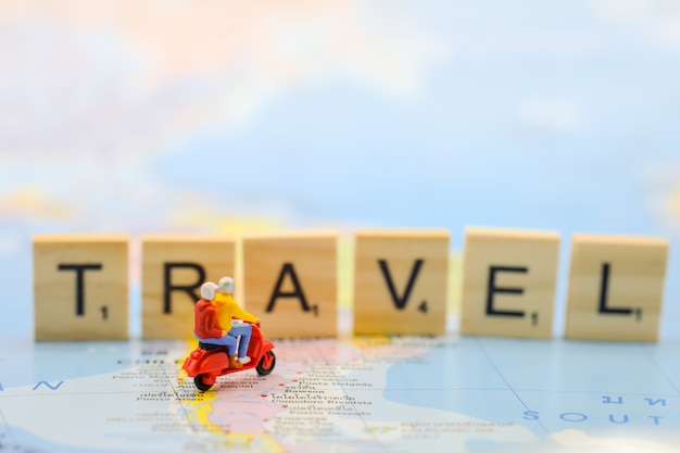 Фото Группа путешественников миниатюрные фигуры ездить на скутере на карте мира с игрушкой деревянных печатных букв.