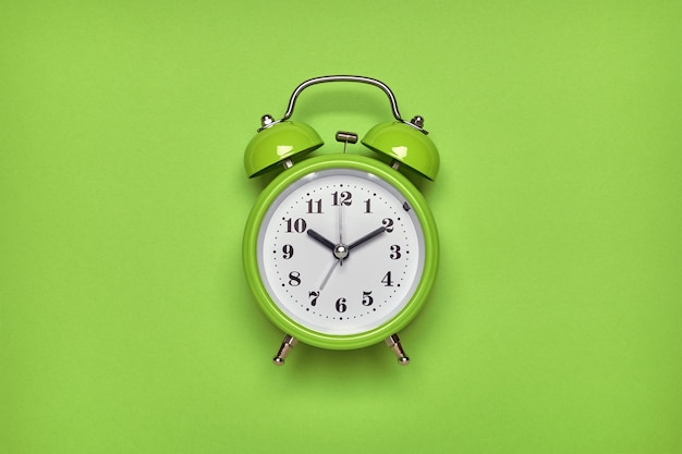 Photo green alarm clock on light green background. top view, flat lay, copy space.