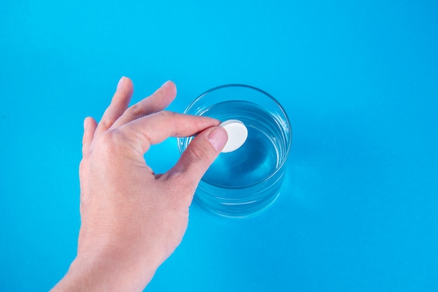 Рука держит шипучую растворимую таблетку и помещает ее в стакан воды
